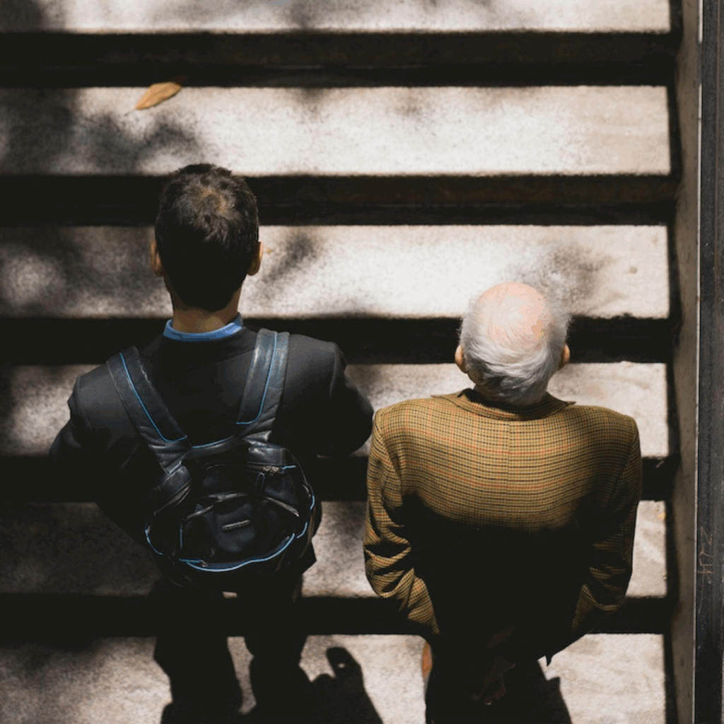 A younger man and an elderly man stand side-by-side before walking up a set of stairs